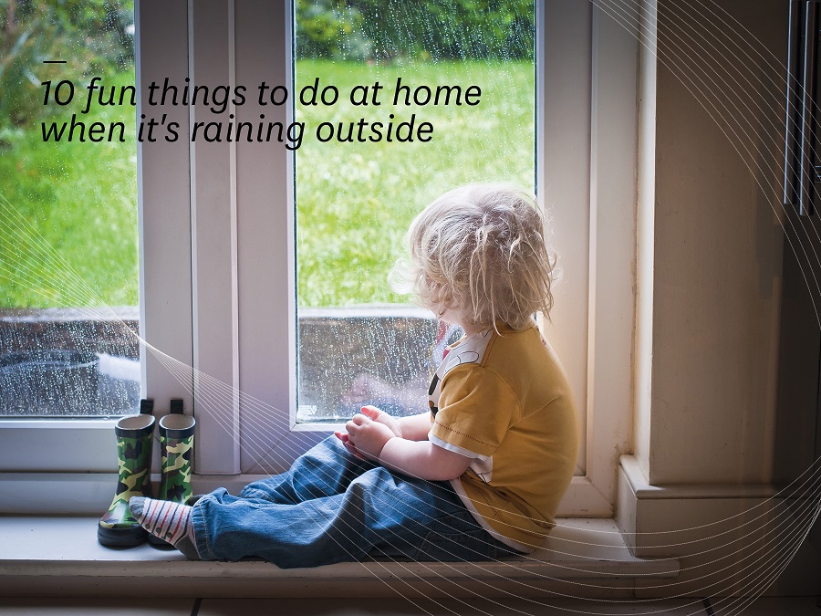 Child sitting on a window ledge looking outside as it rains