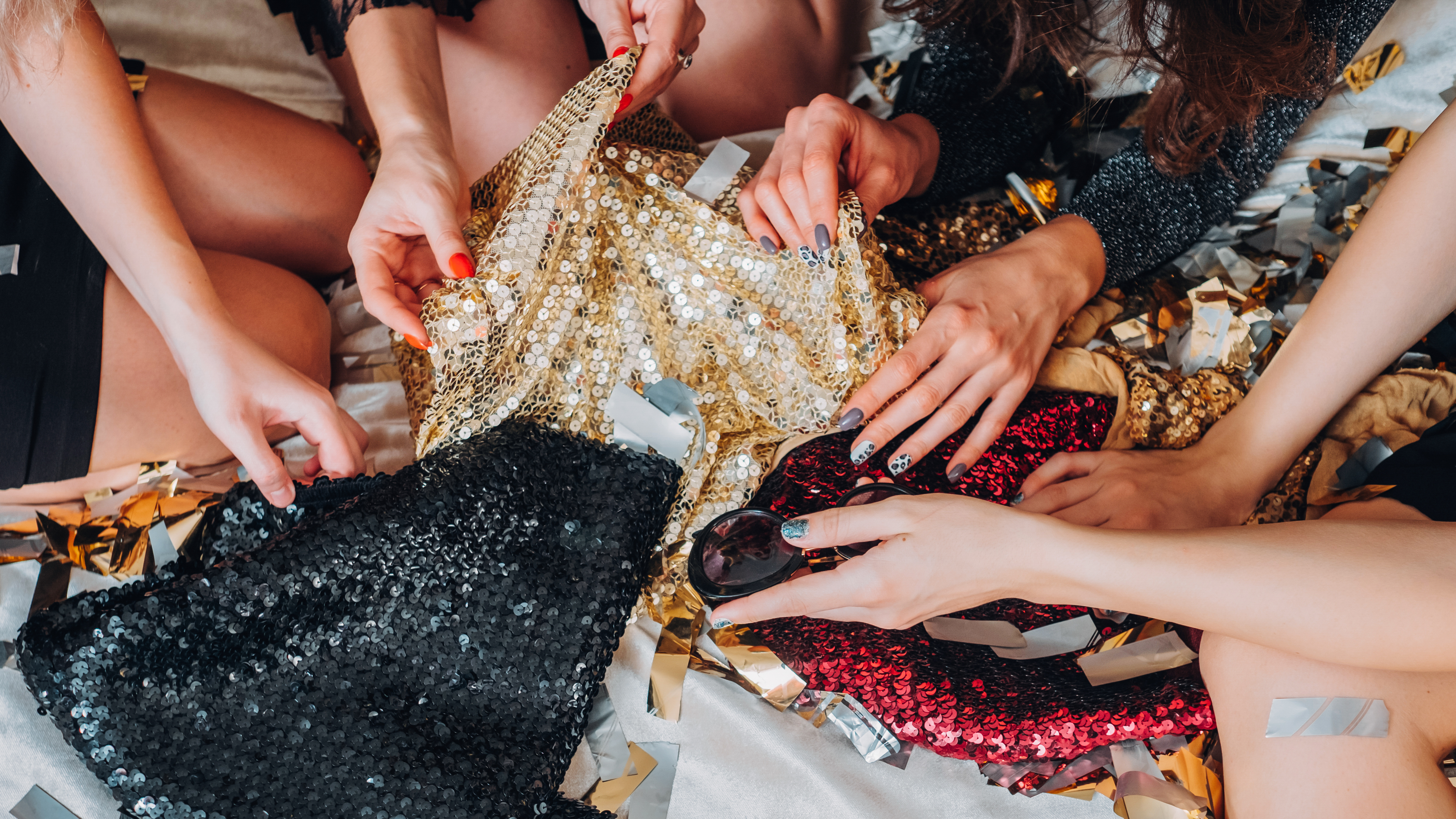 Festive Fashion. Female hands reaching in to grab shiny sequin clothes. 