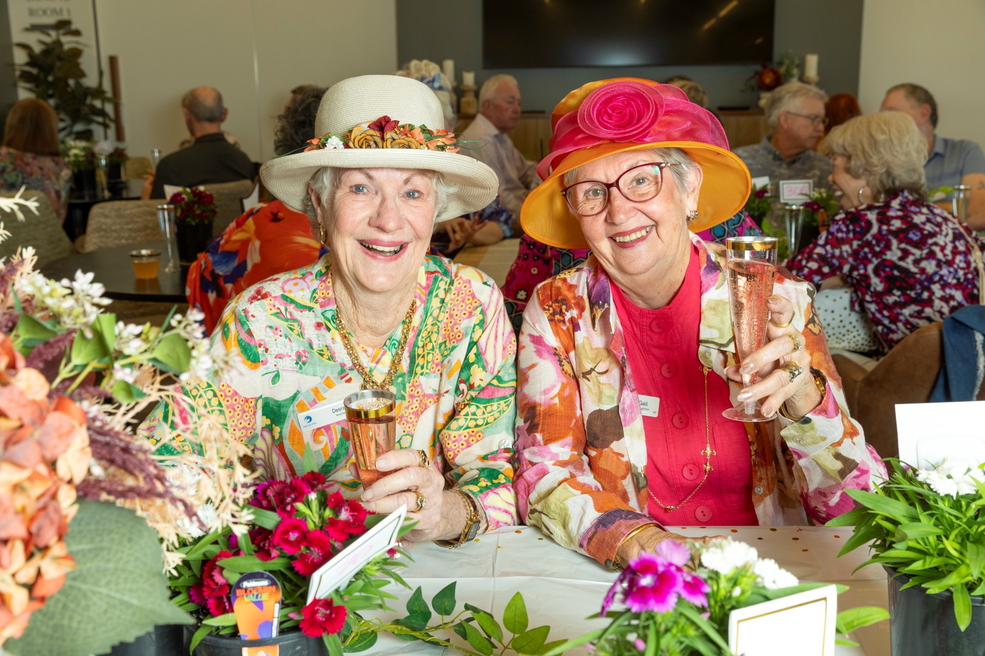 Two women in colourful clothing holding champagne and smiling