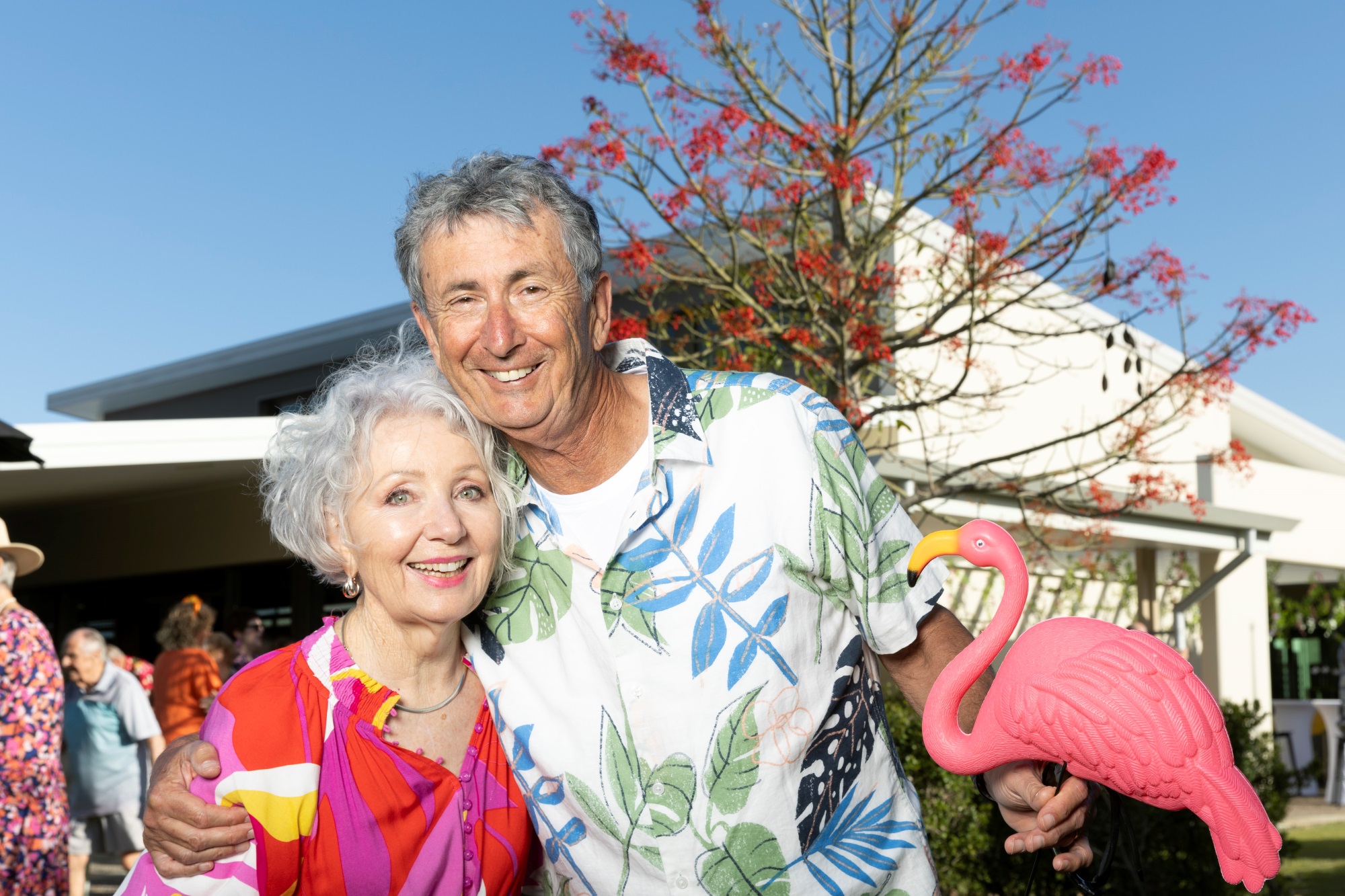 Couple cuddled up together with the woman in a red top and the man holding a plastic flamingo