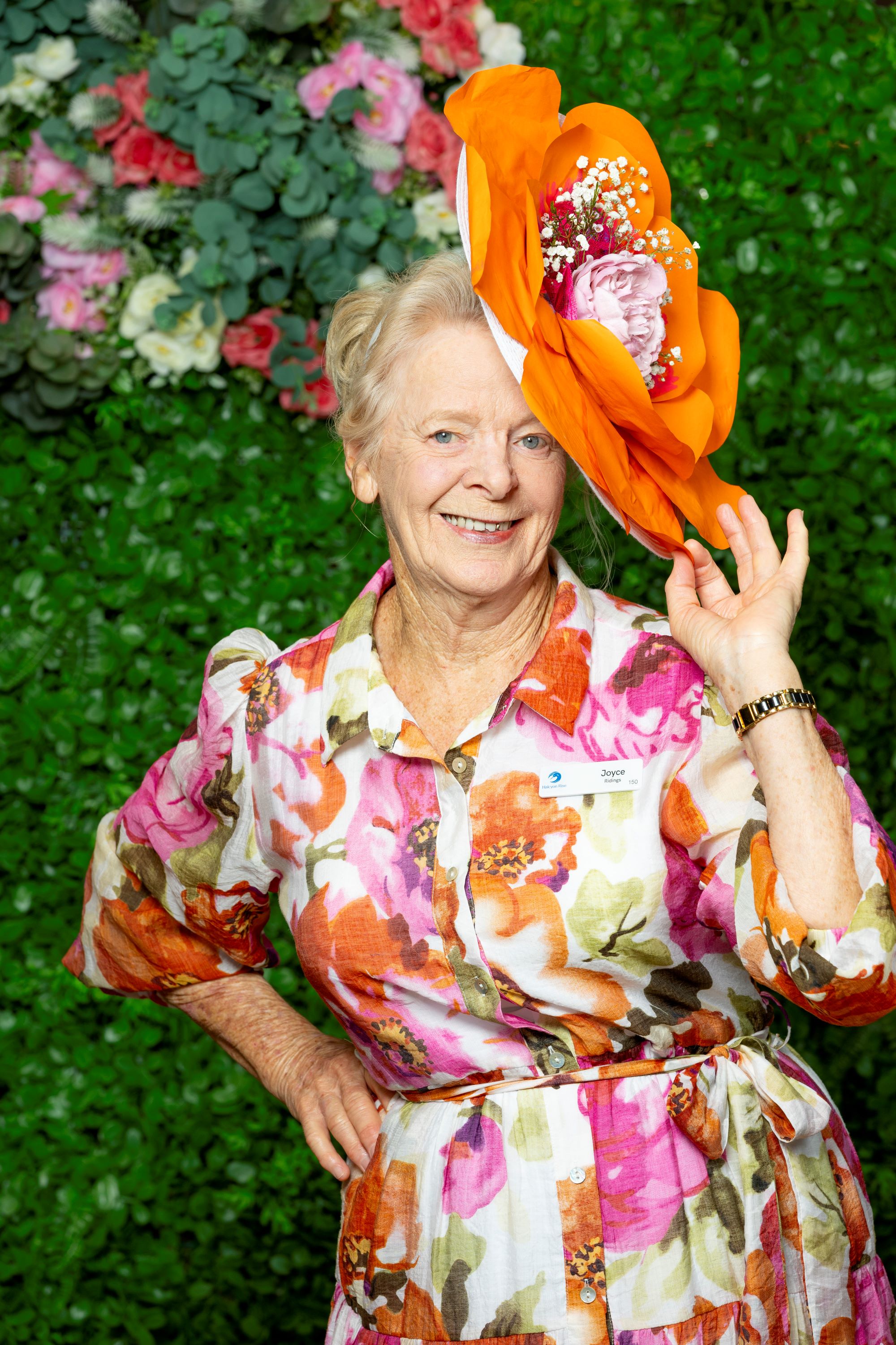 Woman touching her hat while wearing a bright colourful dress and smiling