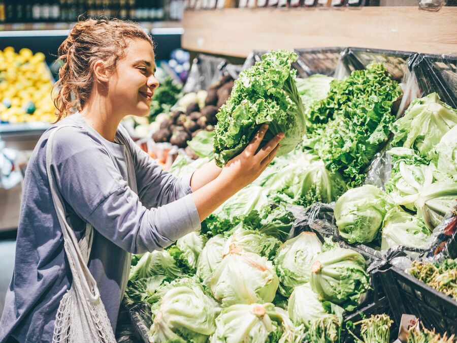 A woman shopping in the produce section of a grocery store holding lettuce.