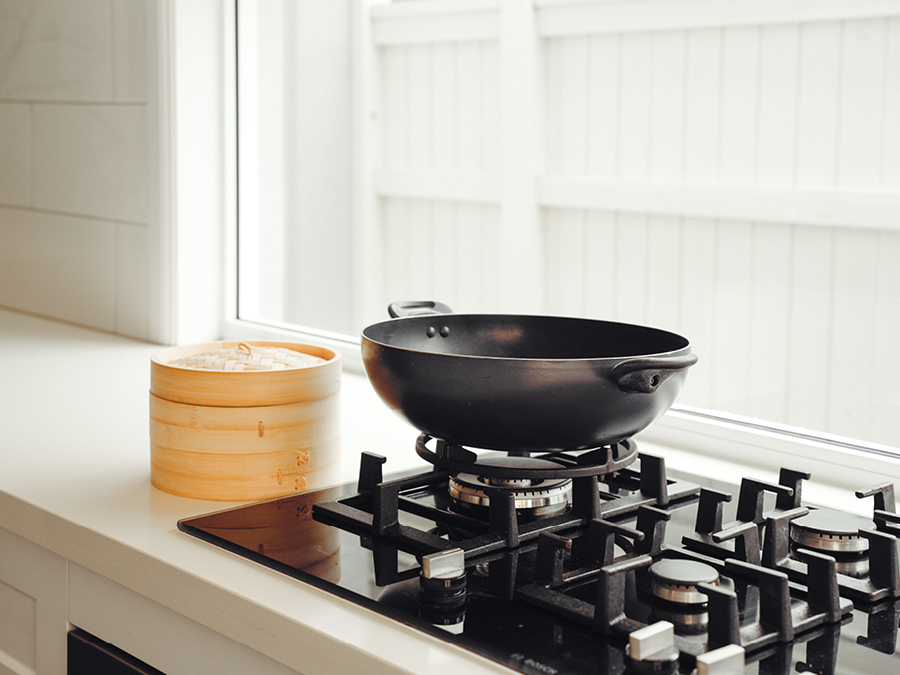 Wok on the stove top with a bamboo steamer next to the stove top