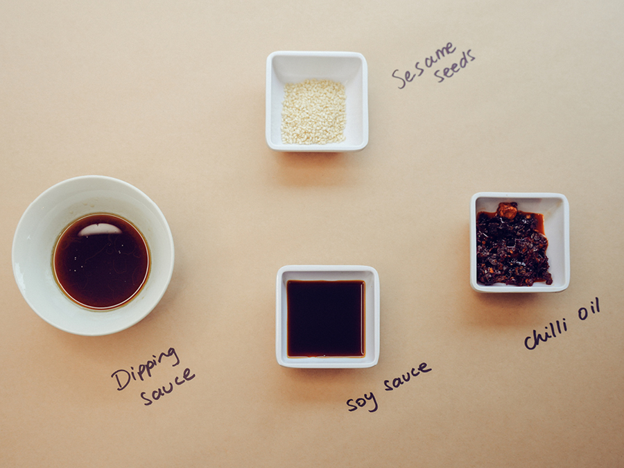 Dipping sauces and side dishes laid out on butcher paper for dumplings