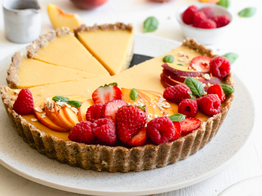 Vegan peach tart topped with seasonal fruit served on a white platter.