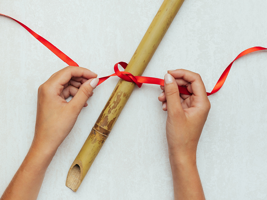 Red ribbon being tied around a bamboo pole.