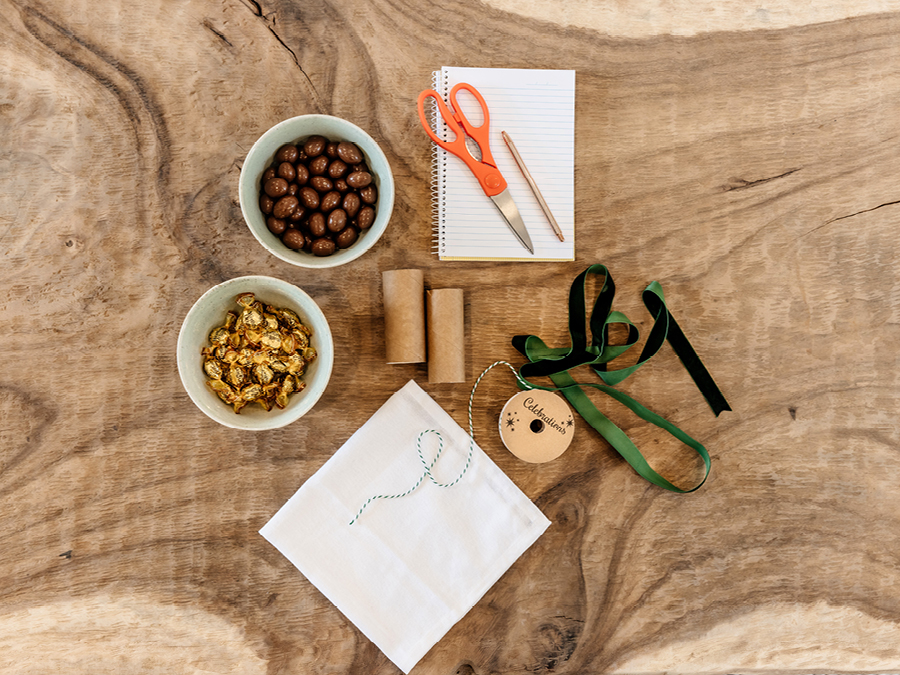 Various items used to create DIY Christmas bon bons including ribbon, prizes, scissors and chocolate