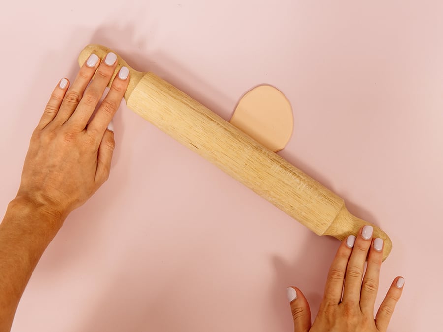 Hands flattening out polymer clay with rolling pin