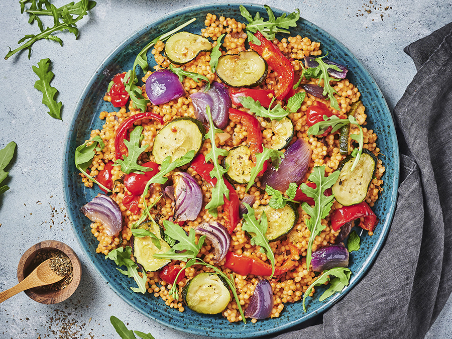 A helthy couscous salad with an assortment of roasted vegetables including zucchinis and red onions, served in a blue bowl. 