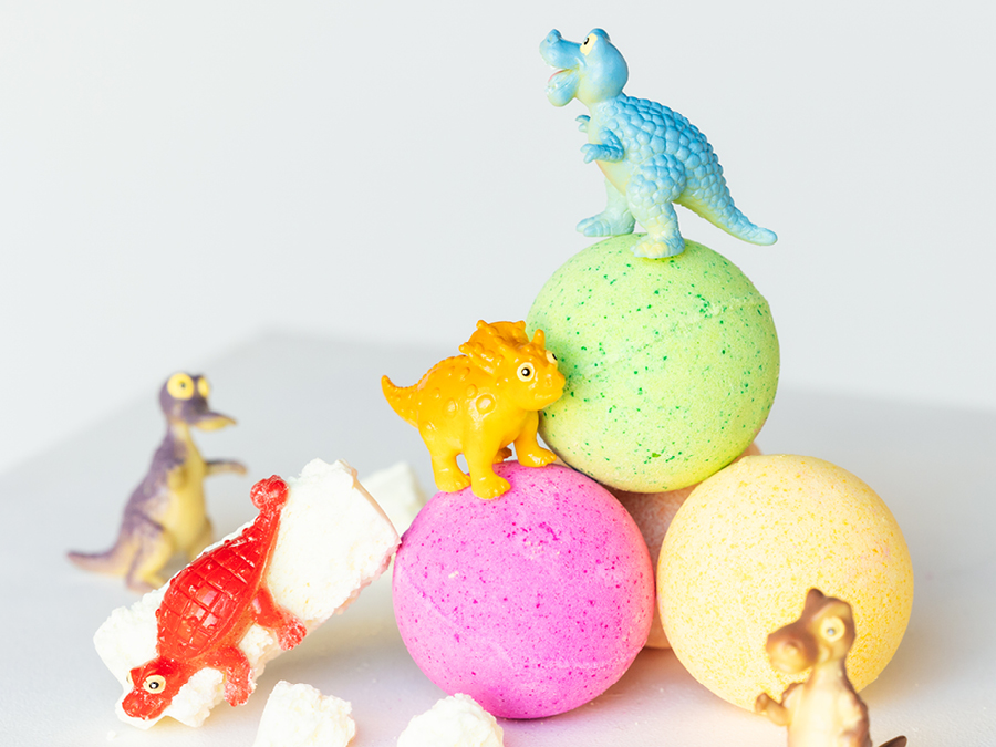 Three DIY bath bombs in different colours stacked together with mini dinosaur figurines. 