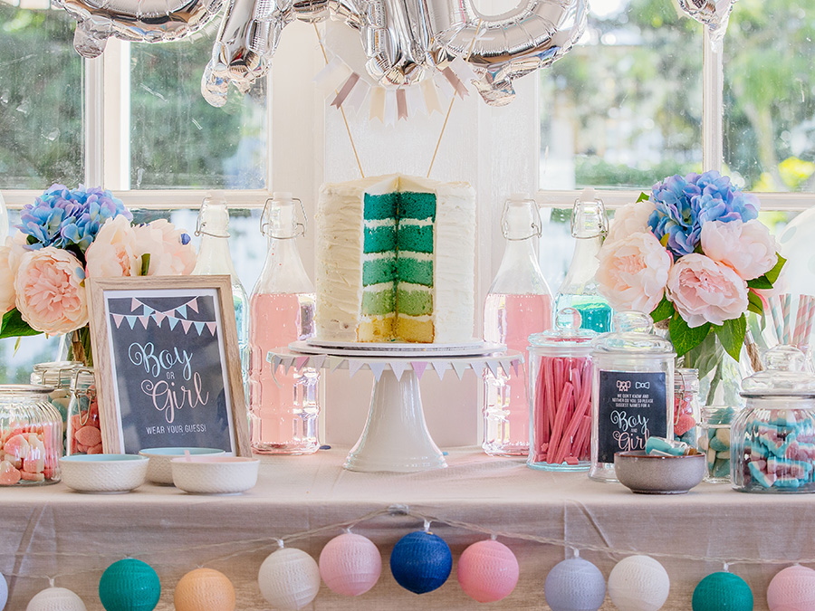 Party decorations, lollies and cake are on a table with gender reveal signage