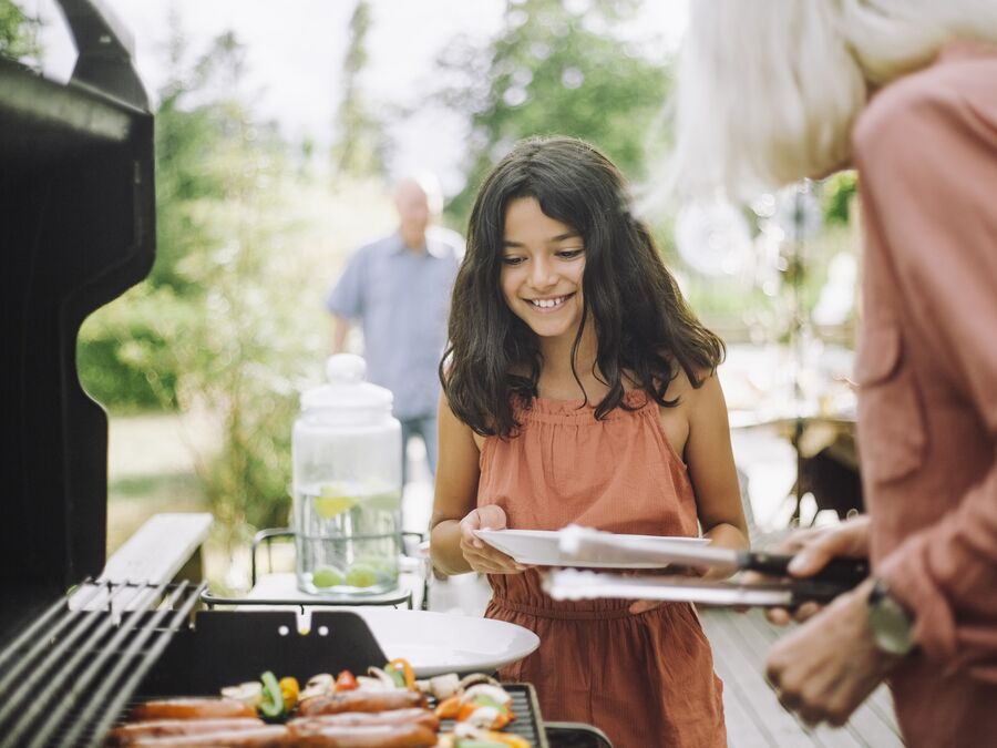 A young girl in an orange dress looking happy as she is being served food from a bbq
