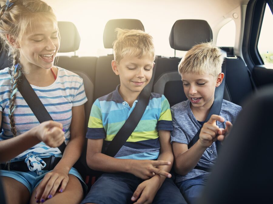 Three kids in the back seat of a car playing 