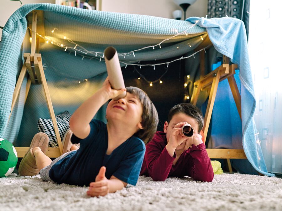 Kids using cardboard tubes as telescopes while laying on the floor in front of a blanket fort