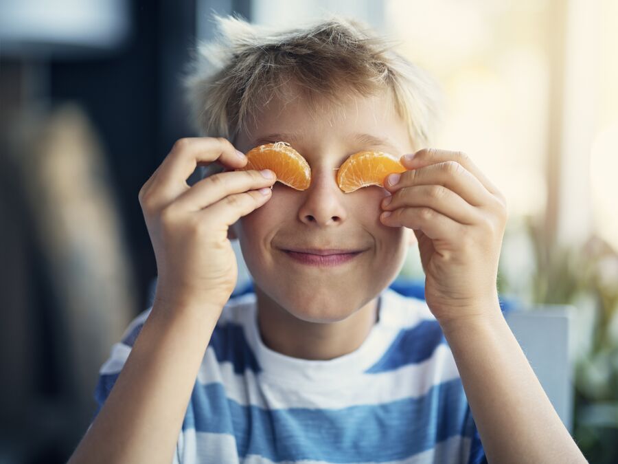 A young boy holding mandarin slices up to cover his eyes.