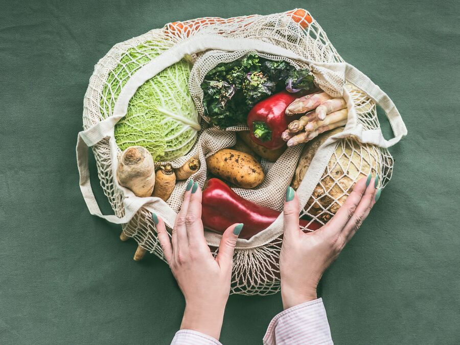 An eco-friendly netted shopping bag holding various fruit and vegetables including capsicum, potato, and cabbage.