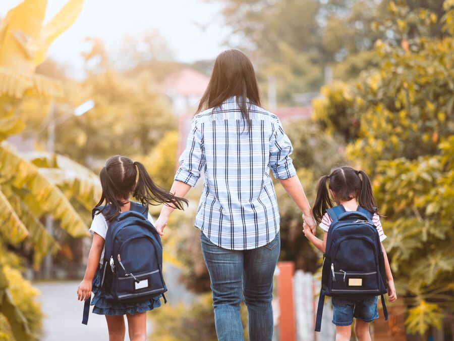 A parent holding the hands of two children going to school